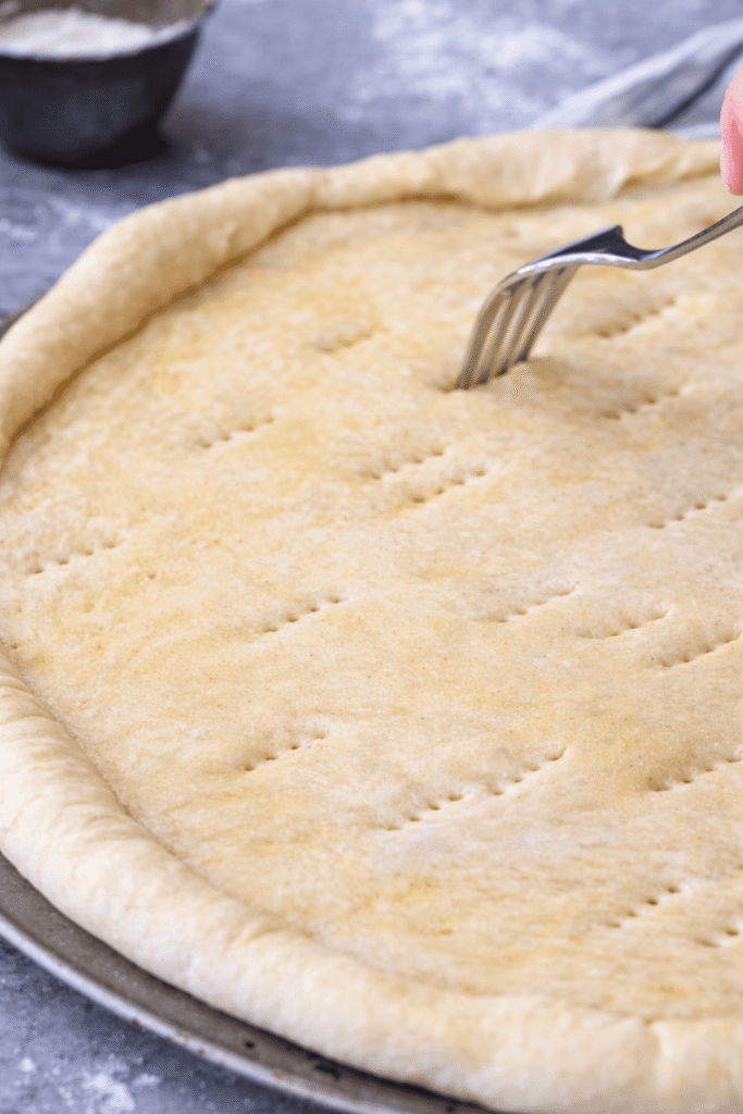Pizzateig wird mit einer Gabel eingestochen, um Blasen beim Backen zu vermeiden
